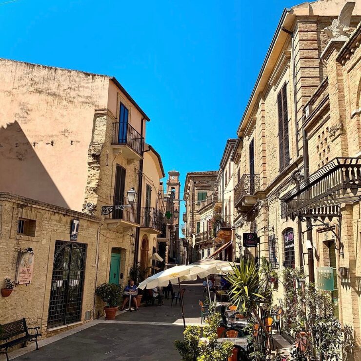Charming street in Crecchio, Italy, with historic buildings, outdoor café tables and narrow alley leading to a church tower