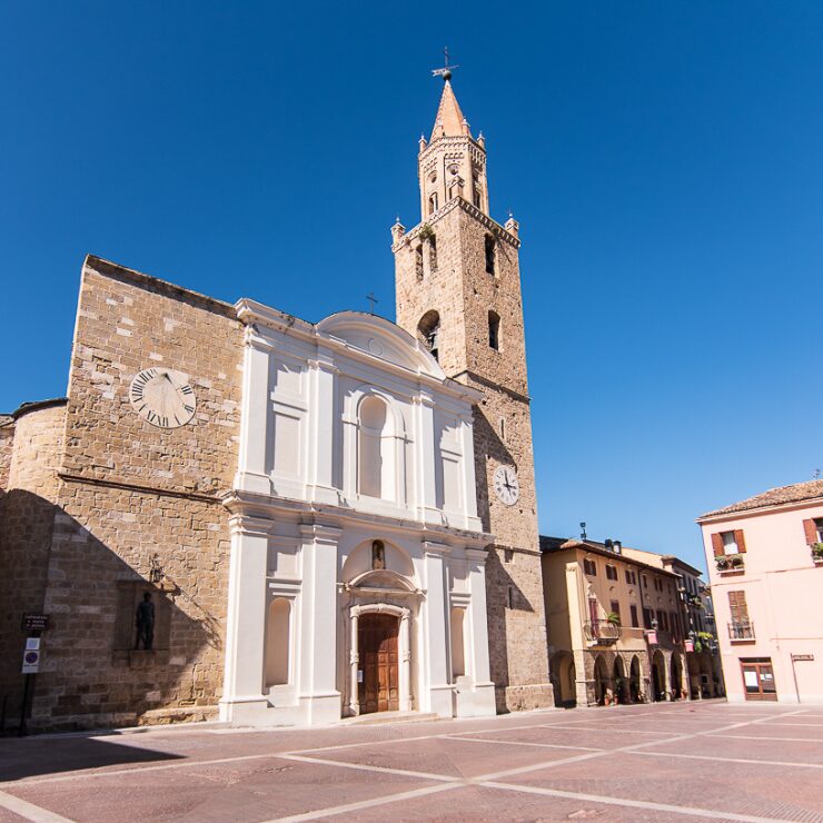 Facciata barocca bianca della cattedrale di una località abruzzese in una piazza soleggiata, con l'alta torre campanaria in mattoni rossastri e una meridiana sul muro laterale sotto un cielo azzurro intenso.