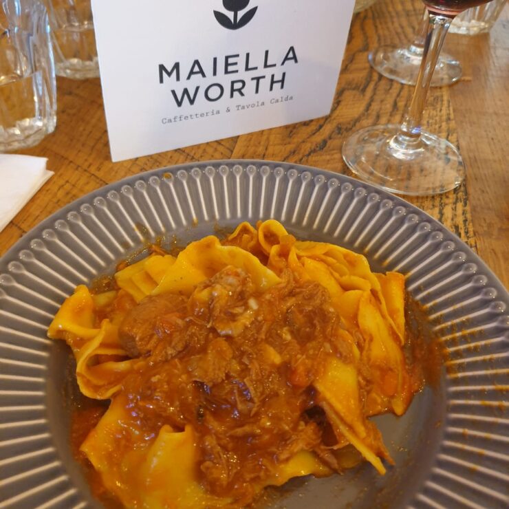 Piatto di pappardelle al ragù servito in un ristorante abruzzese, con il menu di Maiella Worth sullo sfondo