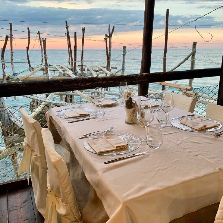 Tavola elegantemente apparecchiata in un ristorante trabocco al tramonto, con vista sul mare Adriatico sulla costa abruzzese