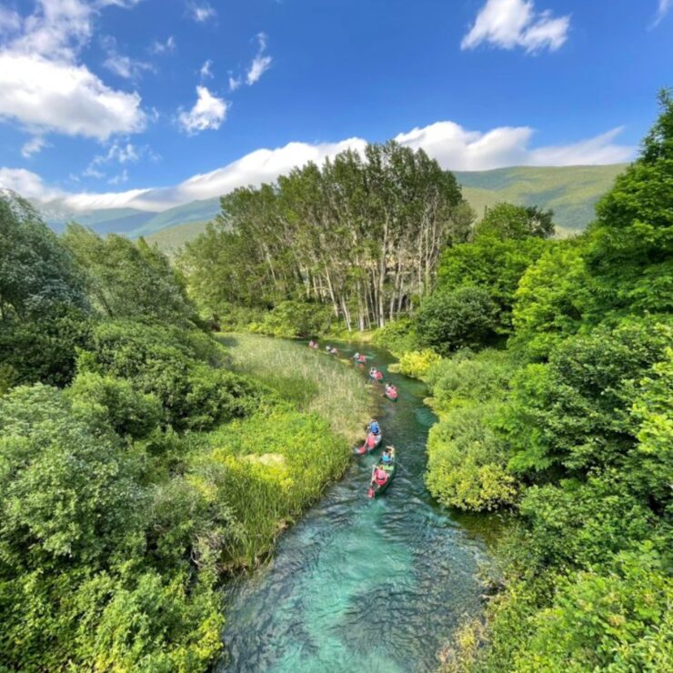 Un grupo de piragüistas navegando por un estrecho río de aguas turquesas rodeado de exuberante vegetación en Abruzzo