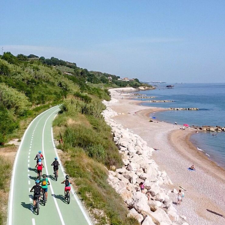 Vista aerea di ciclisti che pedalano lungo una pista ciclabile costiera verde a fianco del mare Adriatico in Abruzzo
