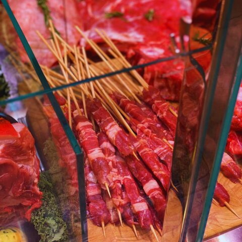 Raw lamb skewers on wooden sticks displayed in a butcher's shop counter in Abruzzo