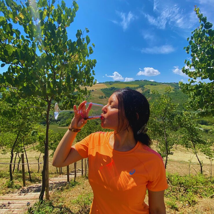 Una donna che beve un bicchiere di vino rosso circondata da vigneti e colline verdi nella campagna abruzzese